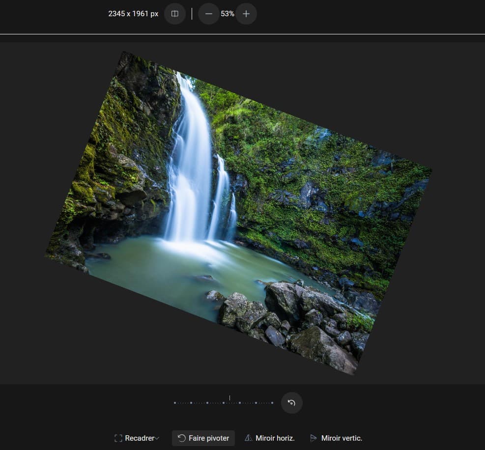 Capture d'écran d'une photo de travers, ouverte dans le panneau des modifications. Dans la partie basse, au centre, une barre graduée pour déterminer le taux d'inclinaison, en-dessous, 4 boutons, "Recadrer", "Faire pivoter" (sur lequel on est), "Miroir horiz." et "Miroir vertic.".