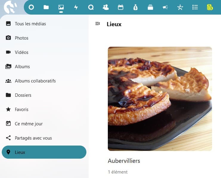 Capture d'écran d'une partie de la page "Lieux". Sur la gauche on voit 10 items, "Tous les médias", "Photos", "Vidéos", "Albums", "Albums collaboratifs", "Dossiers", "Favoris", "Ce même jour", "Partagés avec vous" et "Lieux" qui est sur un fond vert foncé pour le distinguer des autres qui sont sur un fond gris très clair. Sur la droite on voit les 3/4 d'une photo, avec en dessous un lieux cité, Aubervilliers.
